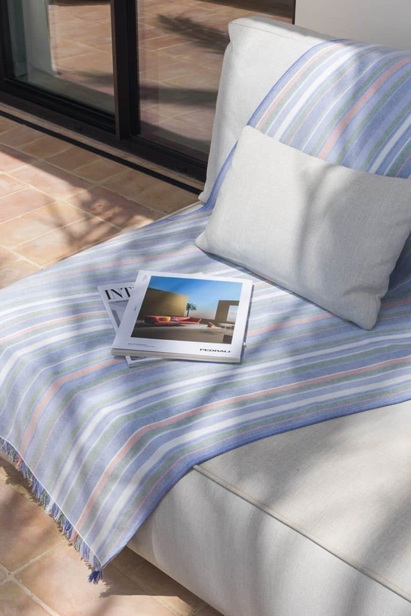 Pareo in blauw-groen-oranje strepen over een daybed met kussens op een terras