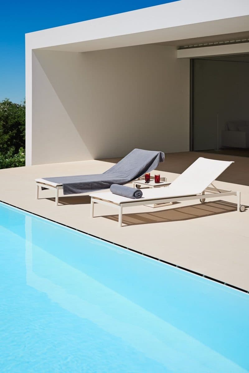 Grijze zwembadhanddoek over een ligbed bij een strak wit poolhouse