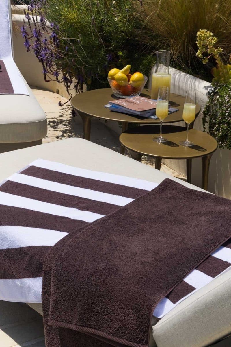 Donkerbruine zwembadhanddoek over een wit ligbed op een zonnig terras