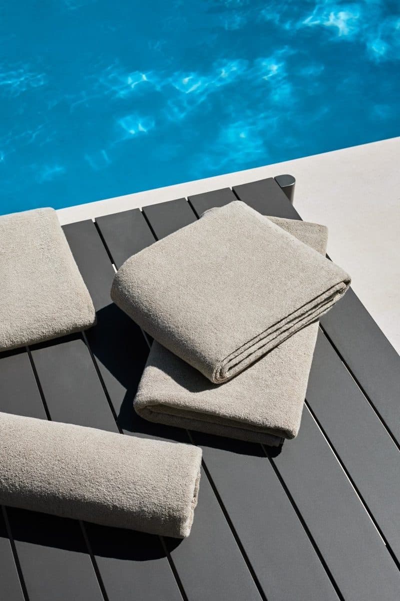 Stapel taupe zwembadhanddoeken op een donker houten terras aan het zwembad