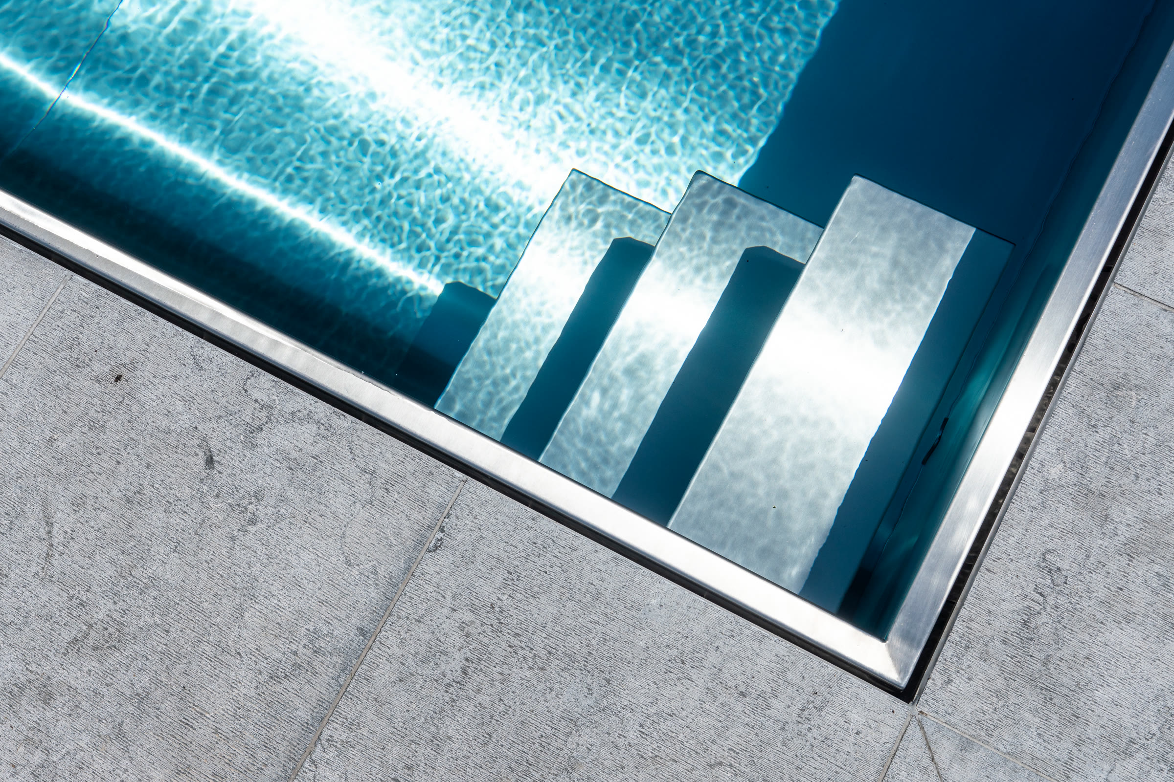 Trap in geborsteld inox die afdaalt in helder zwembadwater, in vol daglicht